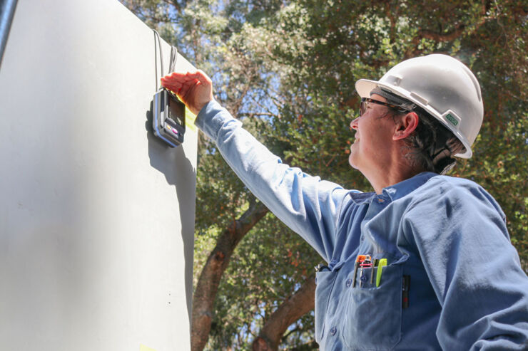 A worker in a hard hat checks a device on the wall