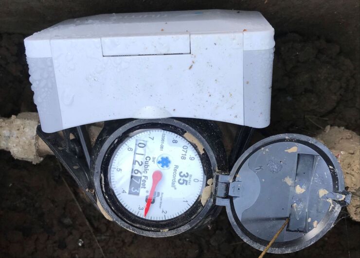 Pictured is a water meter photographed from above with a flowmeter attached to the side.